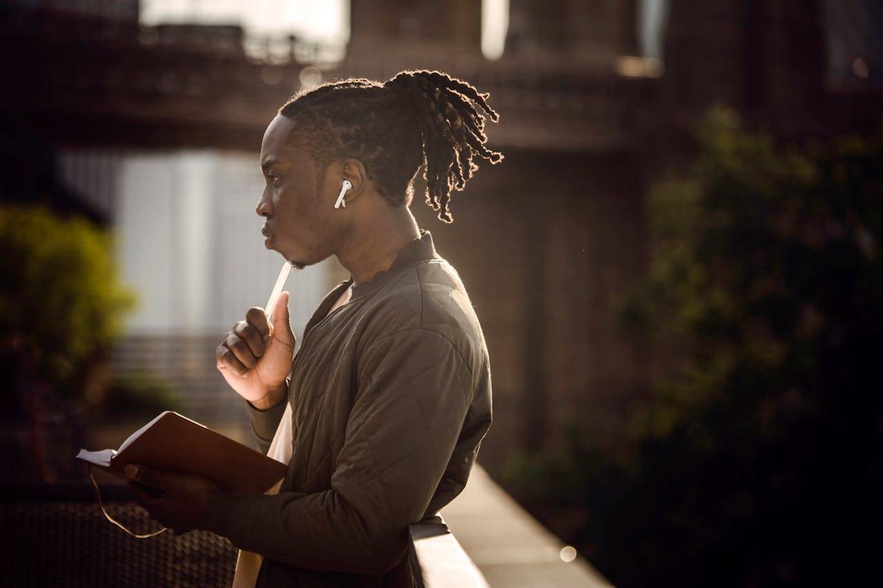 A person with dreadlocks and cornrows, wearing fashionable outerwear, posing in a portrait.